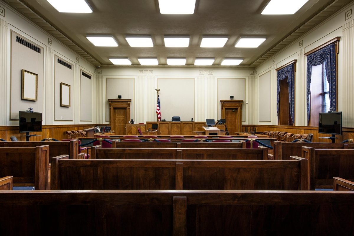 Empty courtroom with wooden gallery benches facing the judge's bench and an American flag